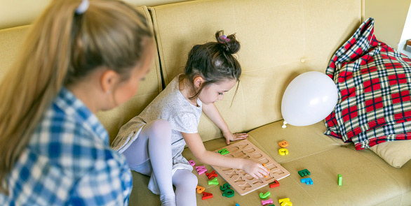 A young single mother is helping her cute little daughter with alphabet learning. Mother is giving her daughter a lesson with an alphabet therapy exercise.