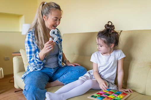 A young single mother is helping her cute little daughter with alphabet learning. Mother is giving her daughter a lesson with an alphabet therapy exercise.