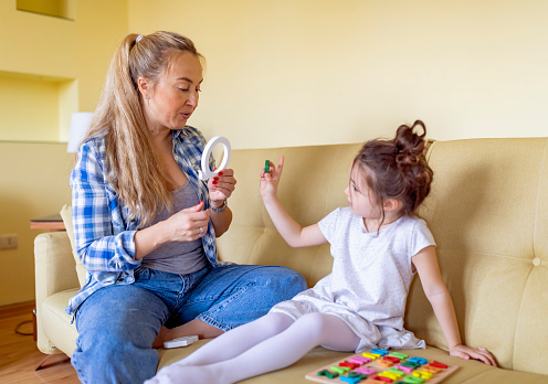 A young single mother is helping her cute little daughter with alphabet learning. Mother is giving her daughter a lesson with an alphabet therapy exercise.