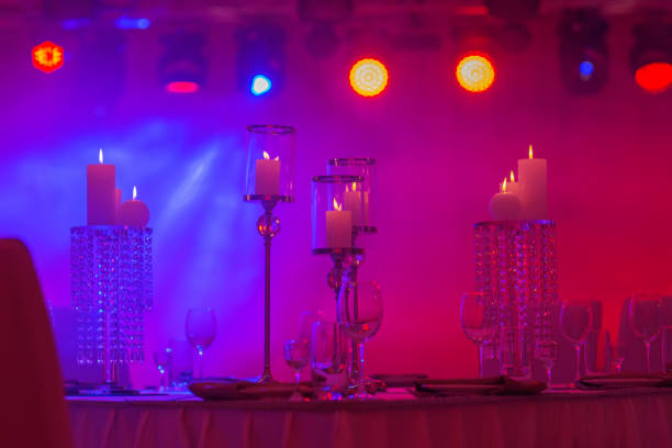 istock Festive table decorated with composition of candles and silver candlesticks in colored light in the banquet hall. Table newlyweds in the banquet area on wedding party. 1194325487