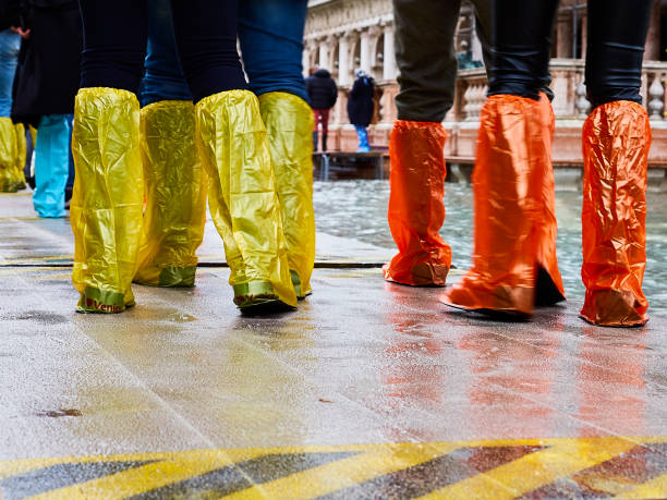 gente caminando con coloridas botas de plástico desechables en pequeñas cubiertas en la plaza inundada de san marco durante la marea de acqua alta high en noviembre en venecia italia - acqua alta fotografías e imágenes de stock
