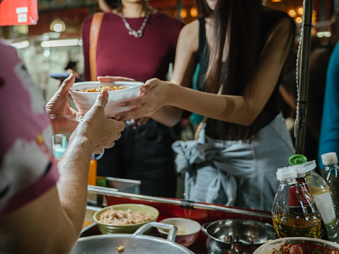 Young tourists buy omelet in a street food marketplace in Bangkok, at Khao San Road