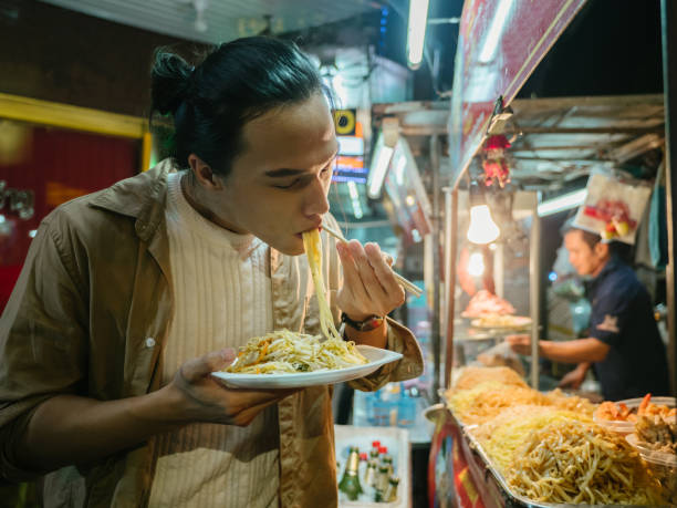 uomo asiatico che si gode la vita del camion di cibo a khao san road. bangkok - thailand thai culture thai cuisine pad thai foto e immagini stock