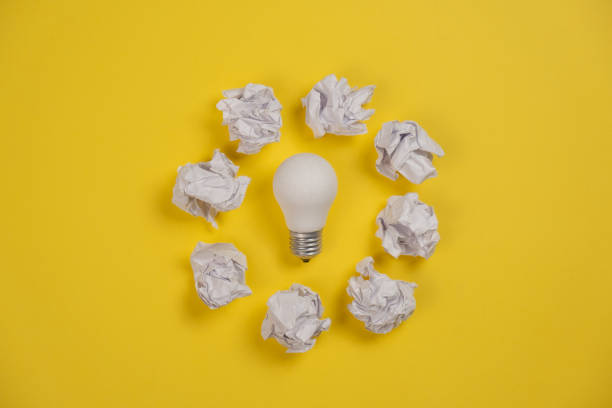 istock Creativity inspiration, great business idea concept with white light bulb and paper crumpled ball on yellow background. Flat lay, top view, copy space 1194337556