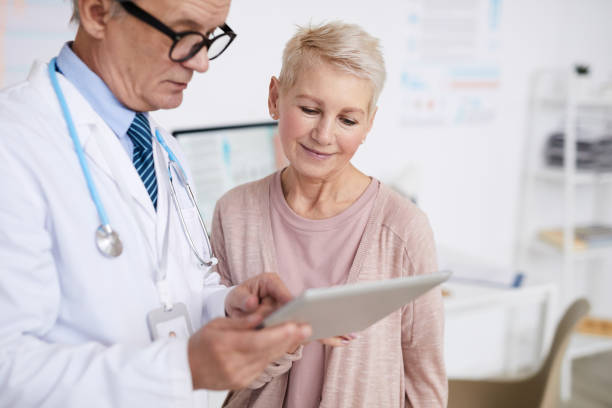 istock Senior practitioner with stethoscope around neck standing in clinic room and answering patients questions according to test results on tablet 1194338376