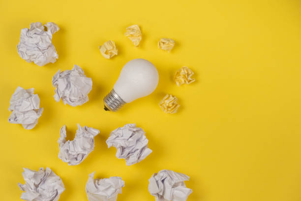 istock Creativity inspiration, great business idea concept with white light bulb and paper crumpled ball on yellow background. Flat lay, top view, copy space 1194339541