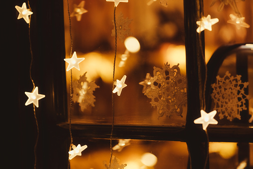 Christmas garland of lights and stars on a window with snowflakes. Reflections and lens flare. Christmas lights background. Festoon glowing in the dark