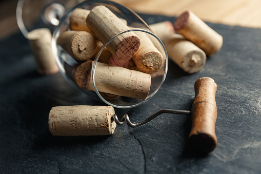 Wine corkscrew with a cork and wine glass full of corks on a black rocky slate background