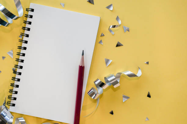 close up top view  empty page of notebook with pencil and rolling silver ribbon on yellow background for happy new year resolution 2020 idea and inspiration concept