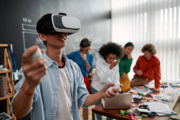 istock The evolution of VR Technologies. Young asian man in casual clothes wearing wearing virtual reality headset and smiling while his colleagues discussing new project behind him. High Tech 1194377871