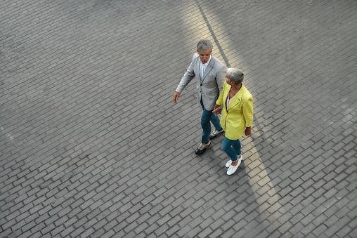 Spending time together. Top view of middle-aged caucasian couple in stylish wear holding hands while walking together through the city street. Relationships. Love concept