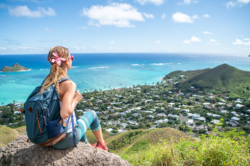 Girl on mountain top overlooking the ocean and the reef on Oahu Island, Hawaii, USA. Woman contemplating the scenic view from hike