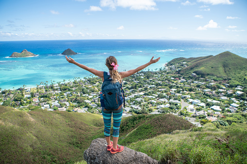 Young woman on mountain top overlooking the ocean arms wide open, Oahu, Hawaii, USA