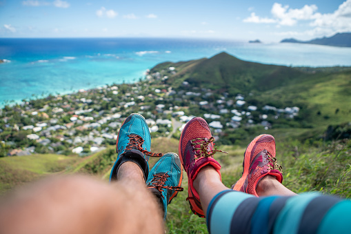 Point of view of couple's feet on mountain top looking at ocean after hiking, personal perspective of couple contemplating nature
