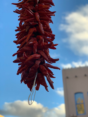 Hanging dry red chile in Santa Fe, New Mexico with blue sky and adobe building in background. Medium shot with no people.