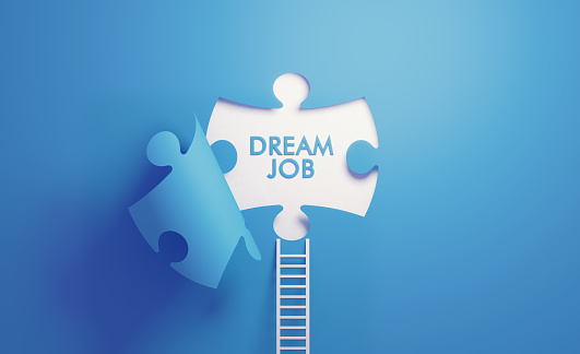 White ladder leaning on blue wall with cut out puzzle shape. Dream job reads inside the puzzle. Horizontal composition with copy space. Career concept.