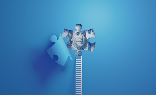 White ladder leaning on blue wall with cut out puzzle shape. One Hundred American Dollar is placed inside the puzzle shape. Horizontal composition with copy space. Solution and finance concept.