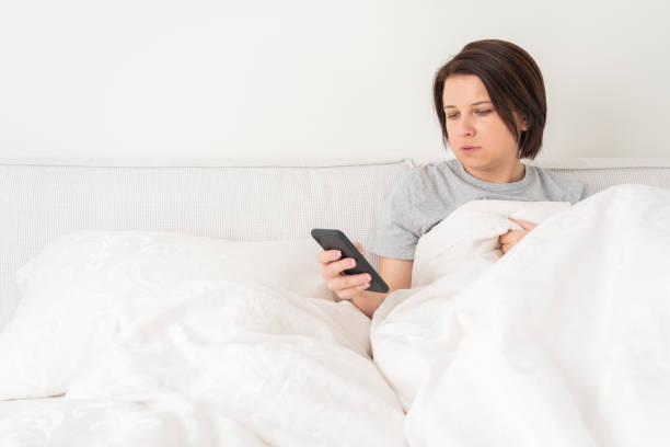 istock Woman using smartphone as she sits in bed covered with duvet 1194401795