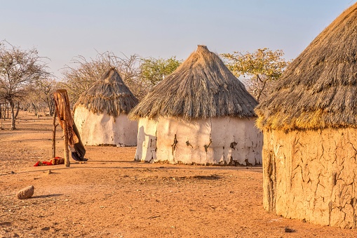 Three traditional, round African houses with thatched roofs in a Himba tribal village in rural Namibia, while clothes hang in the breeze.