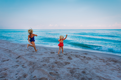 happy little girls run to swim on beach, family beach vacation