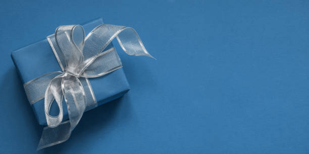 istock Blue giftbox with silver ribbon on classic blue surface. Space for wishes. Birthday card. 1194421737