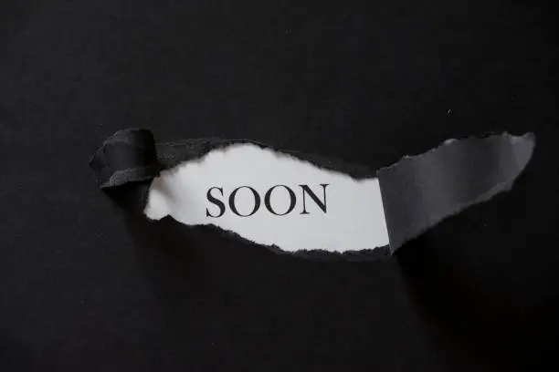 Word SOON printed on a white background with black torn paper.