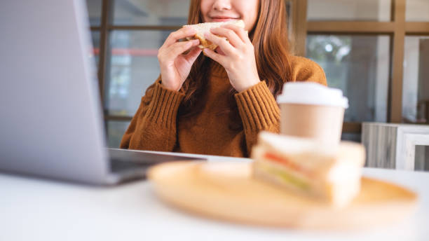 istock woman holding and eating whole wheat sandwich while working on laptop computer 1194428317