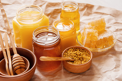 Jars of natural honey bees of different colors, honeycomb and pollen in bowl on table