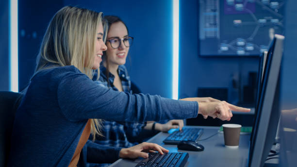zwei weibliche it-programmierer, die auf desktop-computer im rechenzentrum systemkontrollraum arbeiten. team junger profis in der software-und hardware-entwicklung, coding coding - computersprache fotos stock-fotos und bilder