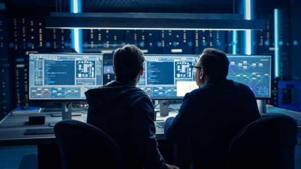Two Professional IT Programers Discussing Blockchain Data Network Architecture Design and Development Shown on Desktop Computer Display. Working Data Center Technical Department with Server Racks dos programadores profesionales de ti que analizan el diseño y el desarrollo de la arquitectura de red de datos de blockchain se muestran en la pantalla del equipo de escritorio. departamento técnico de centros de datos de trabajo con racks de servidores