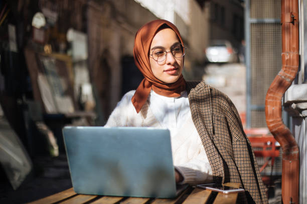 young woman sitting at sidewalk cafe and using laptop - arábia saudita imagens e fotografias de stock