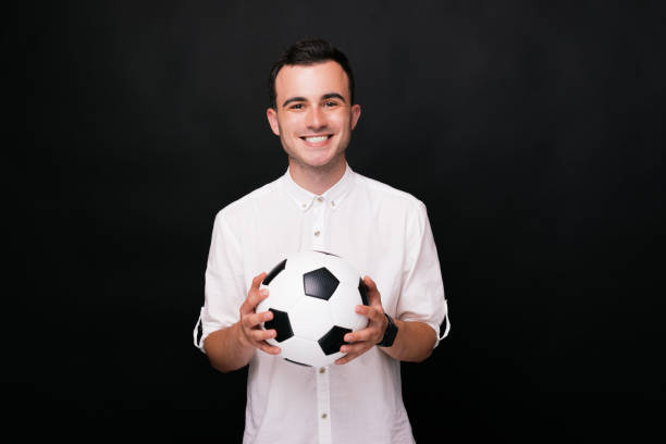 istock Young cheerful man holding a soccer ball with both hands on black background. 1194436912