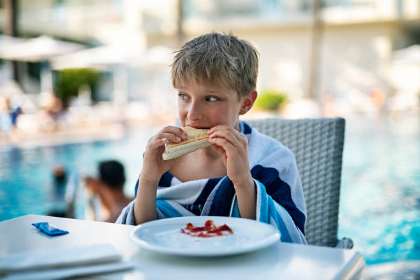 Little boys aged 9 having hot sandwich lunch at pool side table.\nNikon D850
