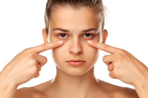 Young woman touching her low eyelids on white background