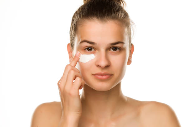 istock A young woman applying cream under her eyes on white background 1194438933