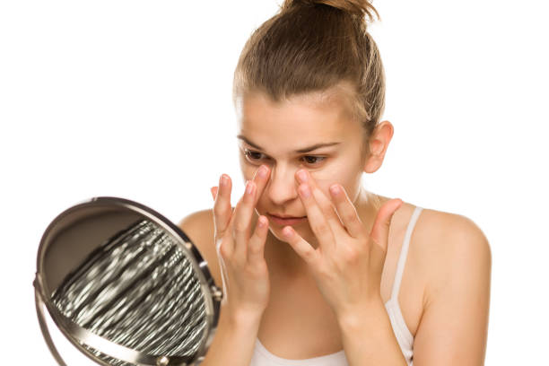 Portrait of young woman applying concealer with her fingers on white background stock photo