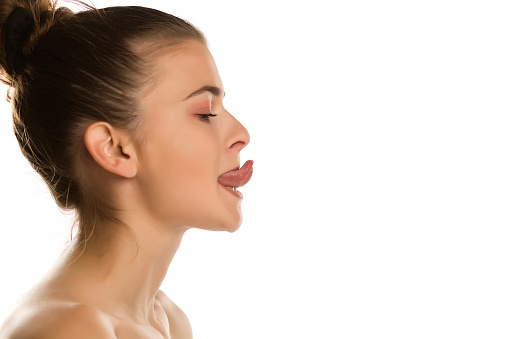Young woman trying to touch the nose with her tougue on white background
