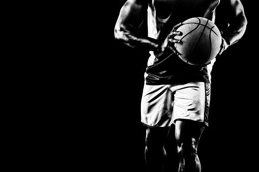 Front view low section of a muscular African American male basketball player wearing team colours stepping forward holding a basketball in two hands