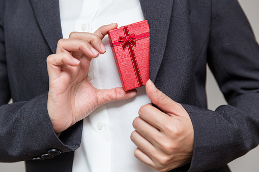 Businessman pulls a gift box out of his suit for giving their company worker for year end big bonus.