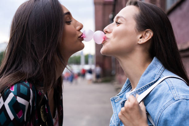 dos jóvenes hermosas chicas hipster sonrientes soplando burbuja con goma de mascar. - chewing gum women bubble blowing fotografías e imágenes de stock