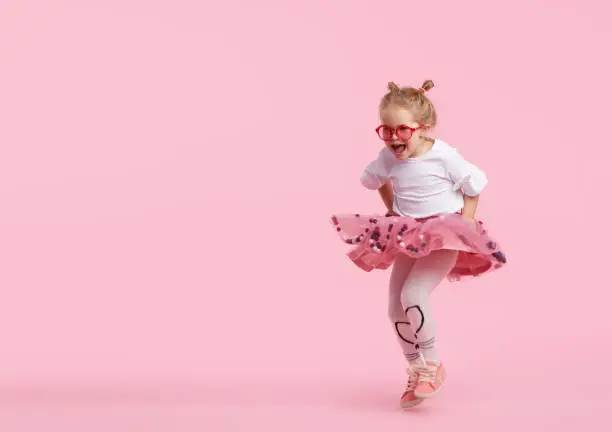 Happy childhood. Funny child girl in tulle skirt jumping and having fun isolated on pink background. Celebrating a vibrant carnival for kids, birthday