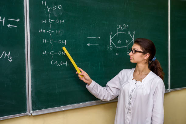 verticale féminine. professeur de chimie restant près du conseil de classe pointant là-dessus - professor adult student chalk drawing formula photos et images de collection