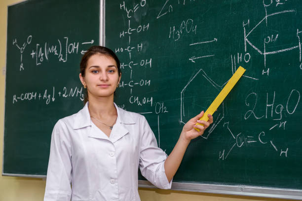 verticale féminine. professeur de chimie restant près du conseil de classe pointant là-dessus - professor adult student chalk drawing formula photos et images de collection