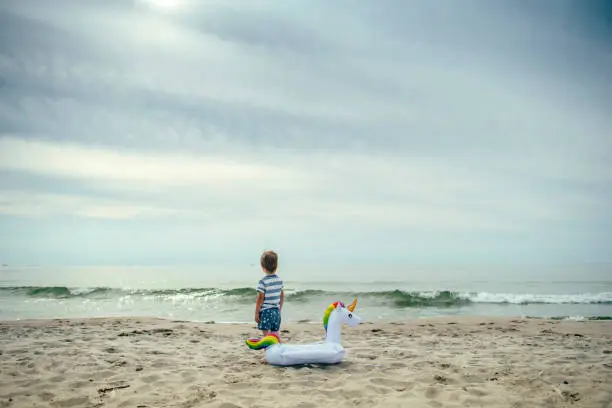 Photo of Happy little boy playing on the beach with a unicorn inflatable ring