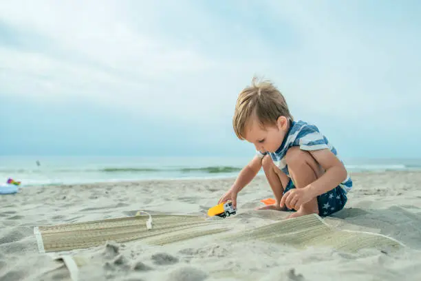Photo of Cute little boy playing with toy car and sand on the beach