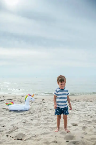 Photo of Happy little boy playing on the beach with a unicorn inflatable ring