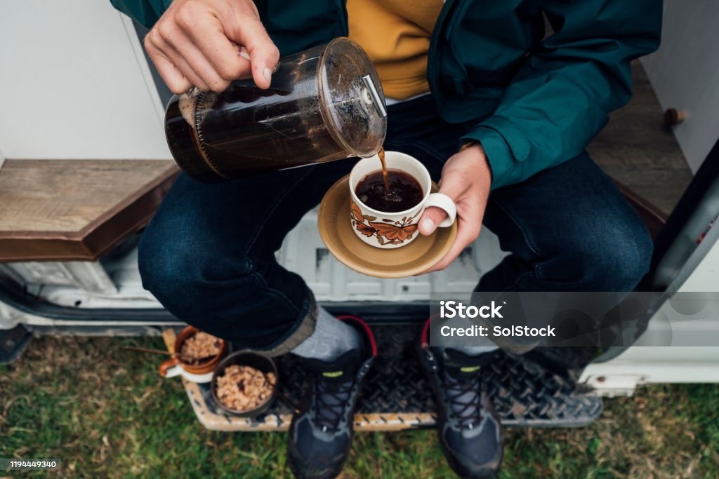 Pouring a Morning Coffee A directly above shot of a young man sitting on the side of his motor home pouring a cup of coffee. Coffee - Drink Stock Photo