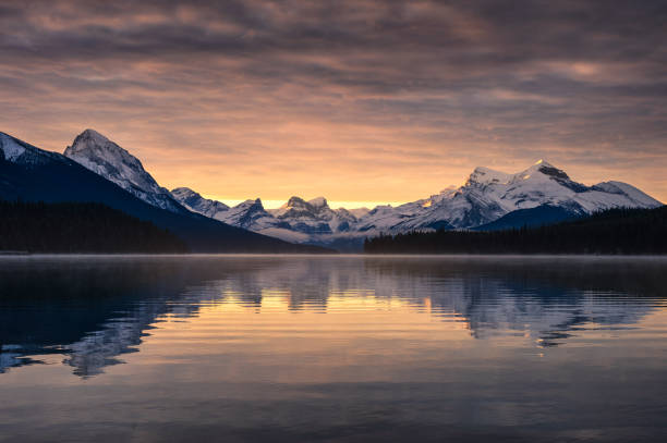 montagne rocciose canadesi con riflessione nebbiosa sul lago maligne e cielo colorato al mattino al parco nazionale di jasper - lago maligne foto e immagini stock