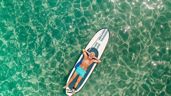 Photo of a senior man relaxing on a paddleboard in the sea