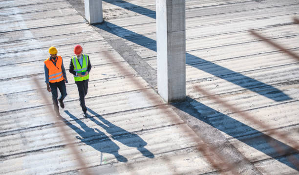 High Angle View of Construction Site Colleagues Elevated view through defocused rebar in foreground of construction site foreman and manager walking and talking. concrete work stock pictures, royalty-free photos & images